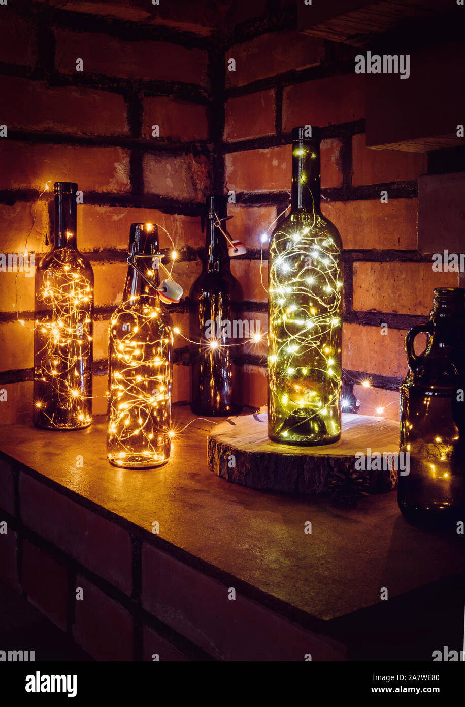 Montón de diferente estilo vintage botellas de cerveza y botellas de vino  verde decorado con cable micro cadena de luces LED en el estante de pared  de ladrillo rojo de fondo. Il
