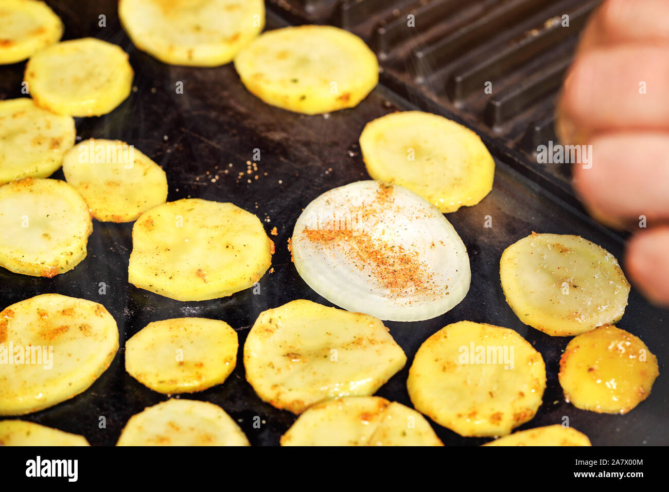 Rodajas de patatas y cebolla condimentada con especias asadas a la parrilla eléctrica, foto en primer plano Foto de stock