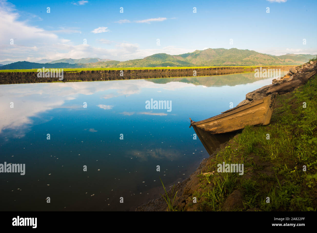 Un lago con una barca abandonada y el agua como un espejo con un hermoso cielo Foto de stock