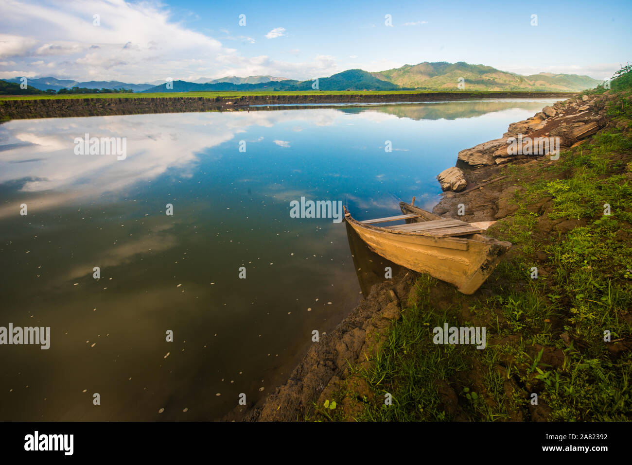 Un lago con una barca abandonada y el agua como un espejo con un hermoso cielo Foto de stock