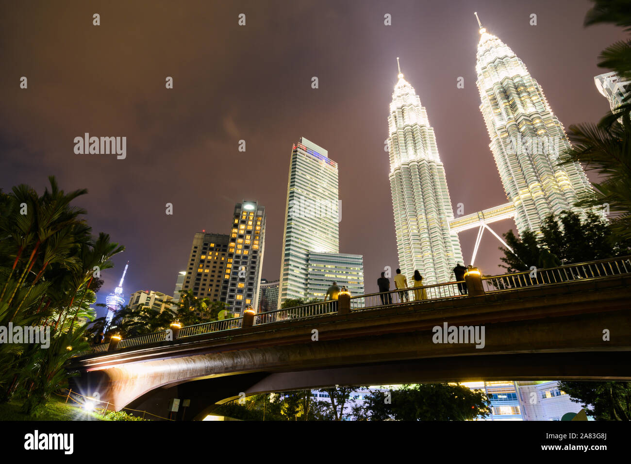 La Torre KL y las Torres Gemelas Petronas iluminada al anochecer. Gente disfrutando de la vista desde un puente en el KLCC Park Foto de stock
