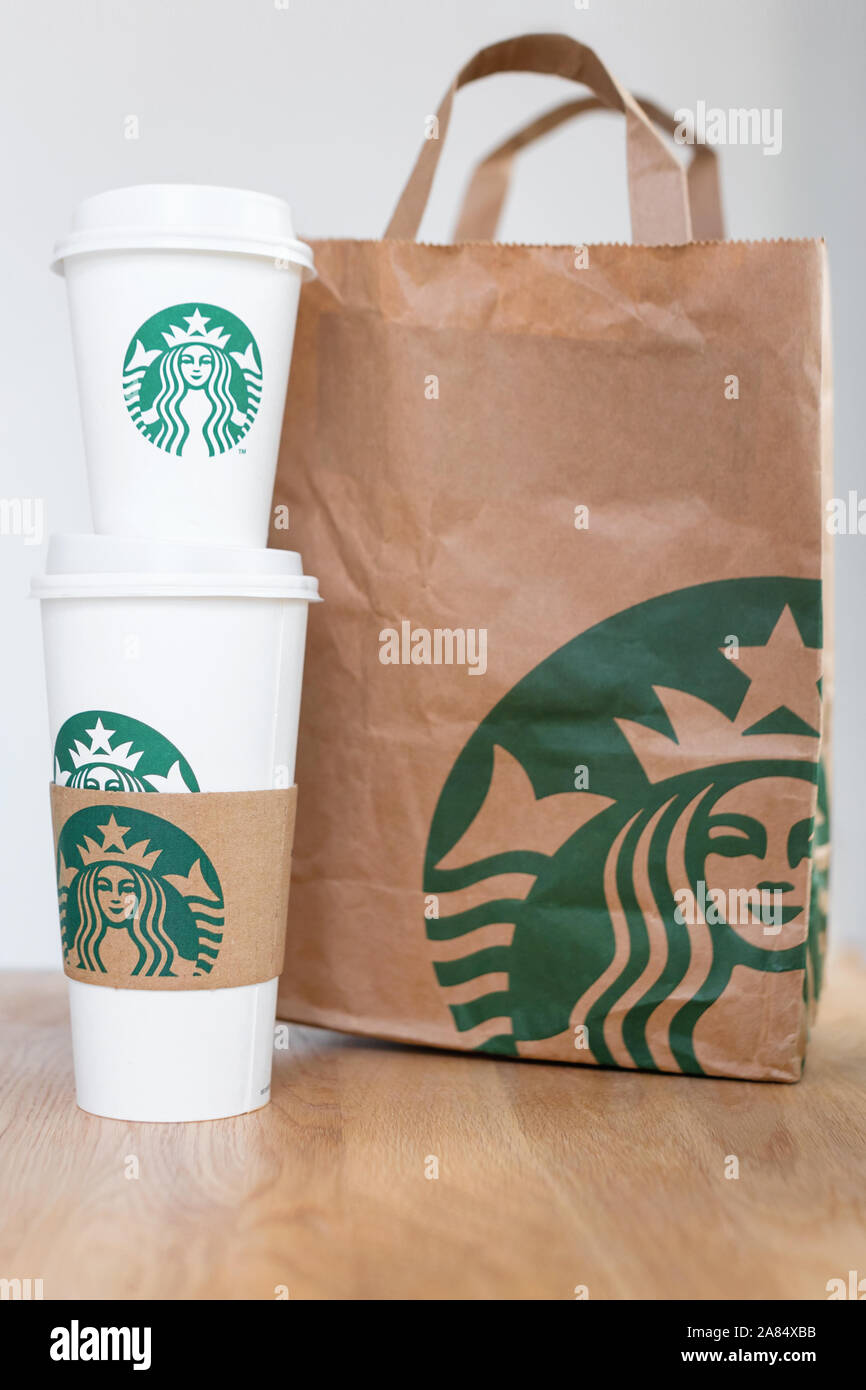 KIEV, Ucrania / Noviembre 06, 2019: café de Starbucks para llevar tazas con bolsa de papel sobre la mesa del contador de madera. American global café y café Foto de stock