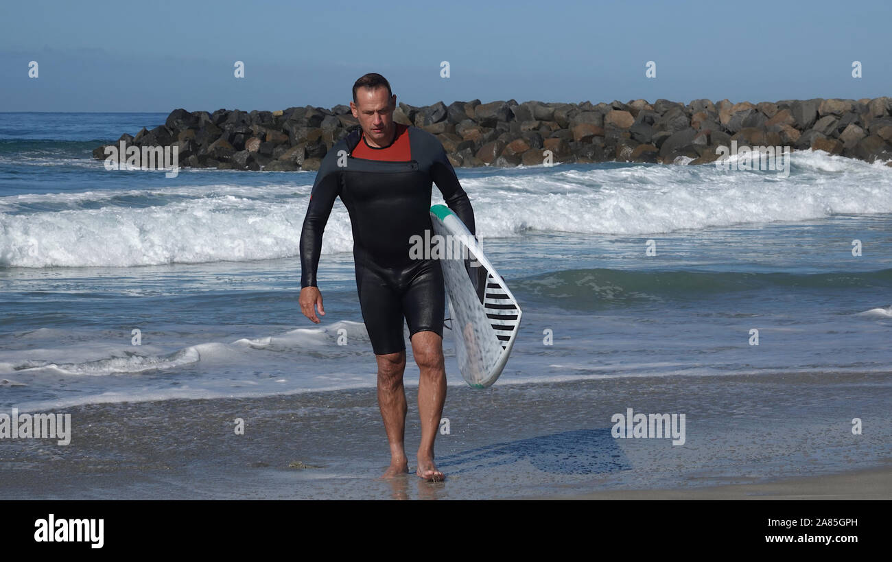 Paddle boarder (Atlético hombre de principios de los 50's) llevando su placa del océano después de una mañana de ejercicio Foto de stock