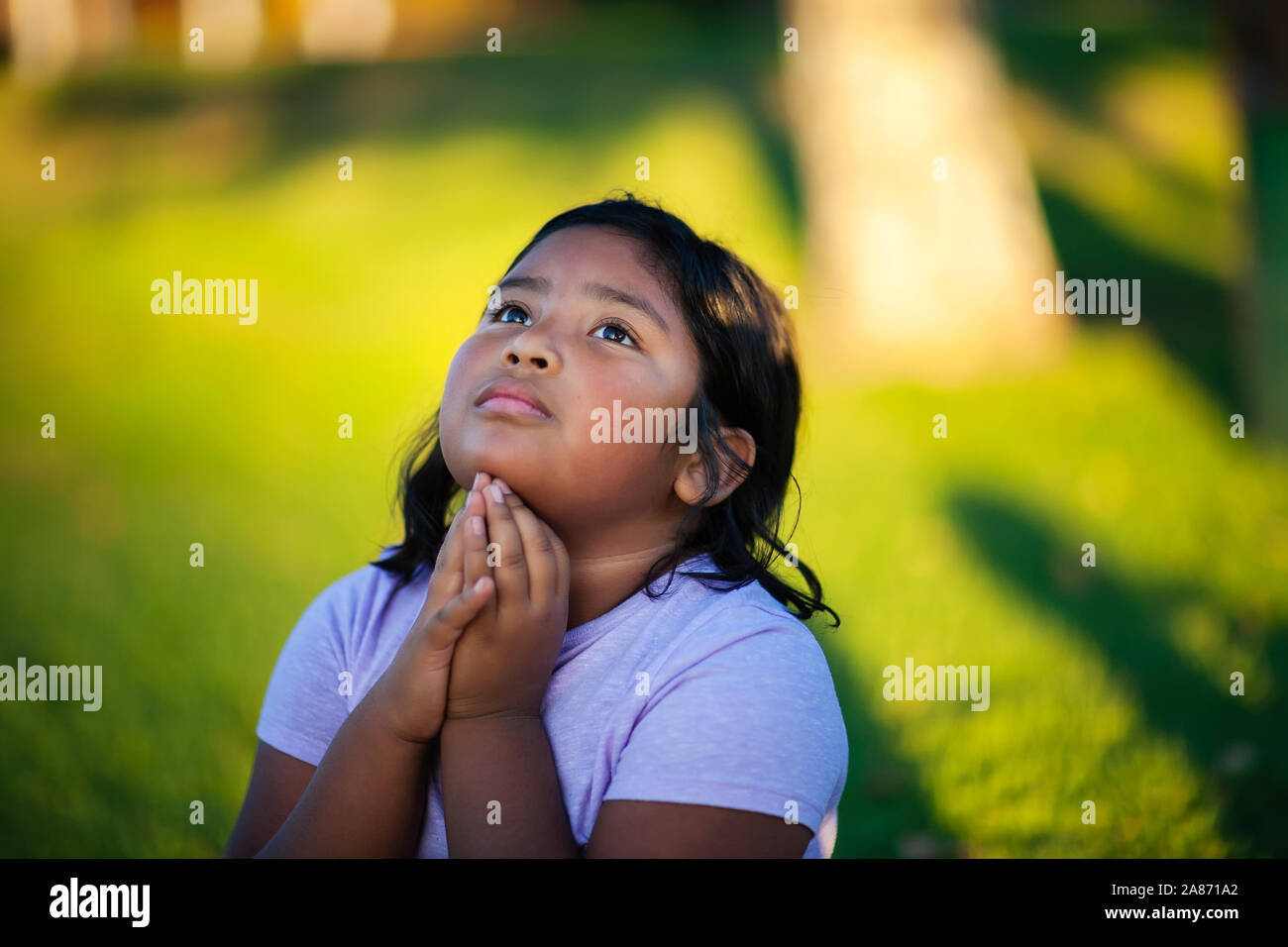 Una niña latina con fuerte convicción hacia Dios, se arrodilla a rezar en la súplica a Dios el Altísimo. Foto de stock