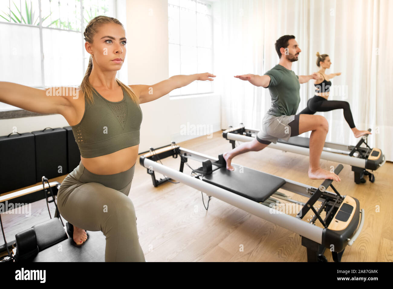 Las personas que trabajan fuera haciendo yoga alta lunge ejercicios sobre pilates reformador camas en un gimnasio en un concepto de salud y fitness Foto de stock