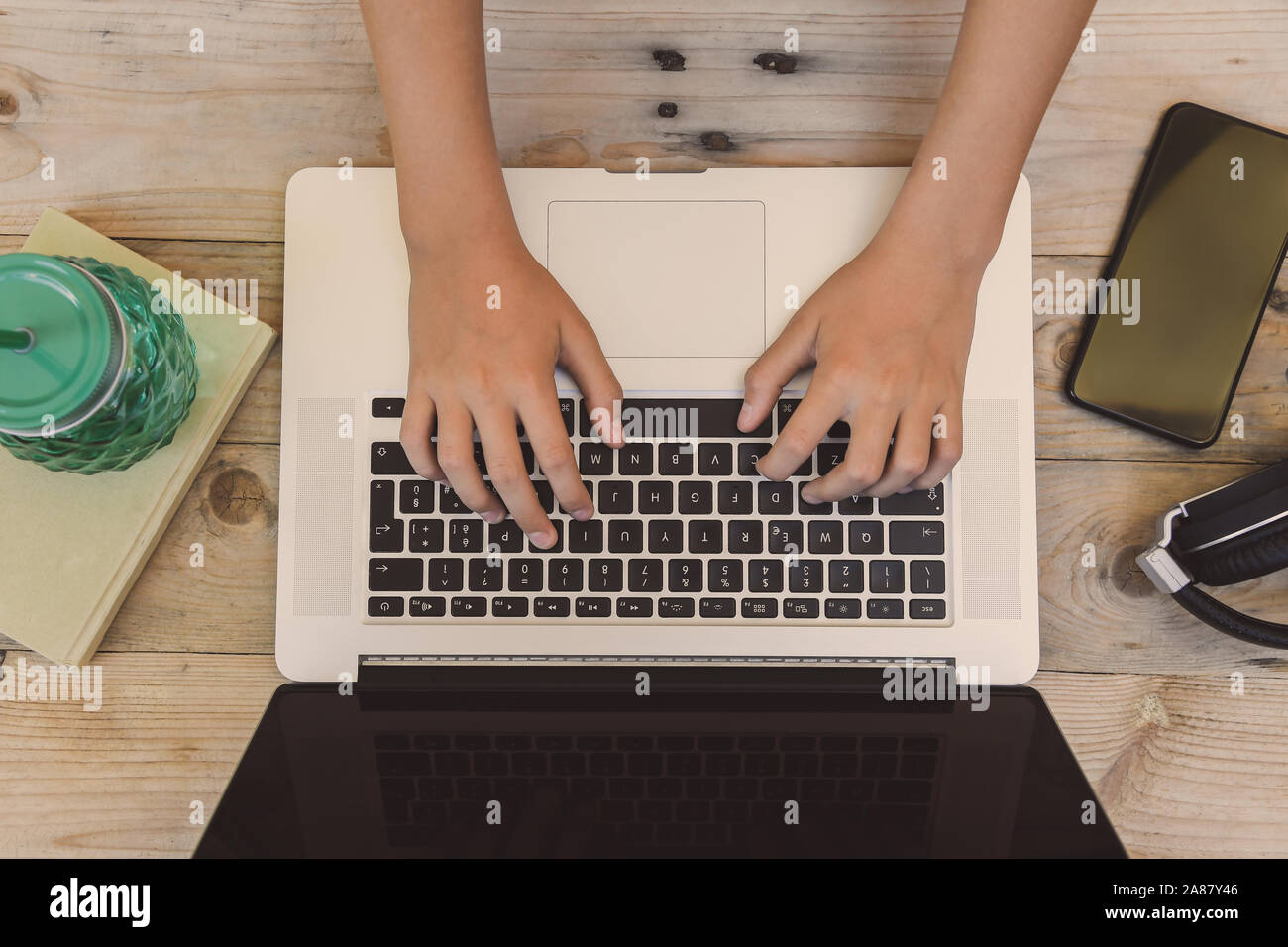 Las manos de un joven escribiendo en un teclado portátil sobre una mesa de  madera rústica. Teen utilizando un ordenador para descargar buena música en  su smartphone. Adolescente Fotografía de stock -