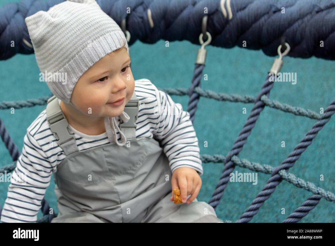 retrasar angustia conectar Retrato de un pequeño bebé chico chica cerca. El niño camina en el patio de  recreo, montando un nido swing. Mono impermeable gris y gorro de punto, Kid  10 Fotografía de stock -