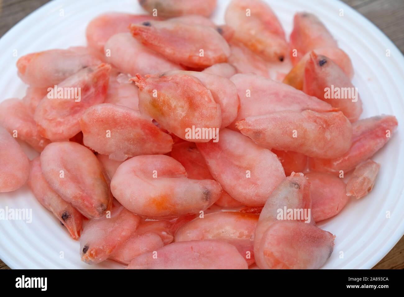 Camarones cocidos congelados acostarse sobre una placa blanca. Camarones en  hielo glaseado se deshielan en una placa Fotografía de stock - Alamy