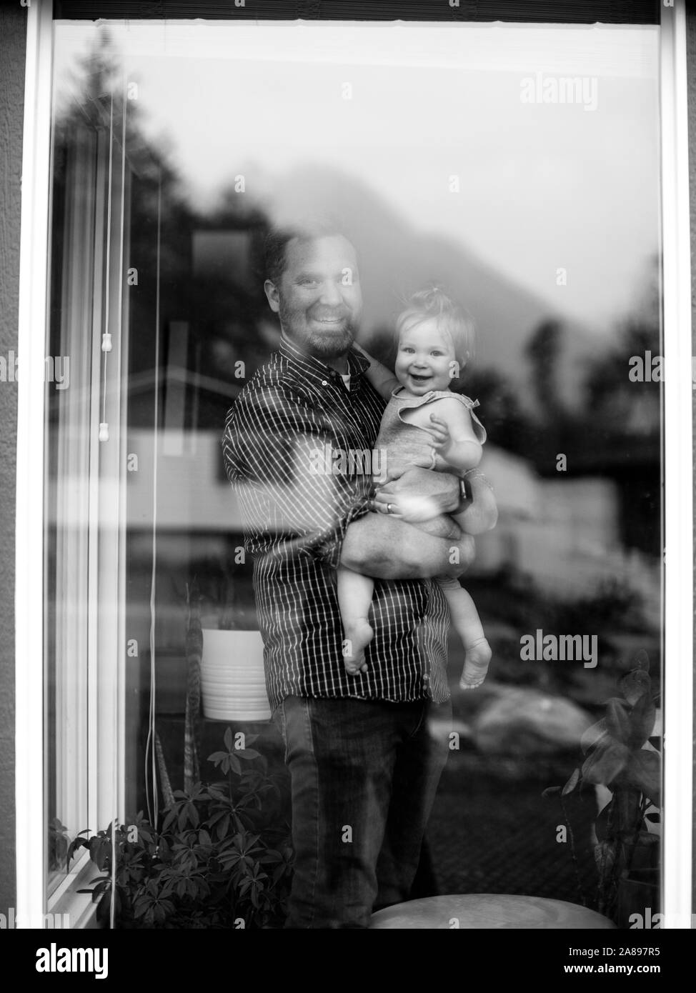 Padre sosteniendo a su hija detrás de la ventana Foto de stock