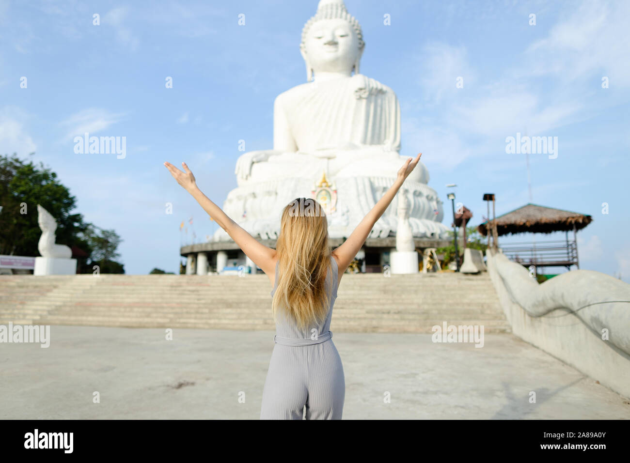 Mujer joven con los brazos estirados de pie cerca de hormigón estatua de Buda en Phuket. Foto de stock
