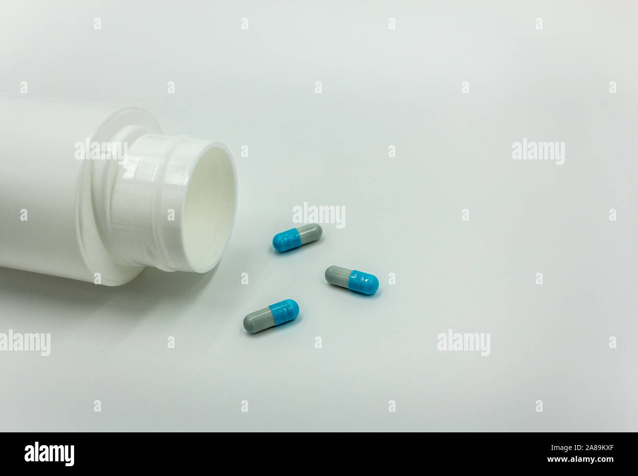 Cápsulas de medicamentos en un cuadro blanco junto a un bote de pastillas vacío - Fondo blanco, espacio para texto Foto de stock