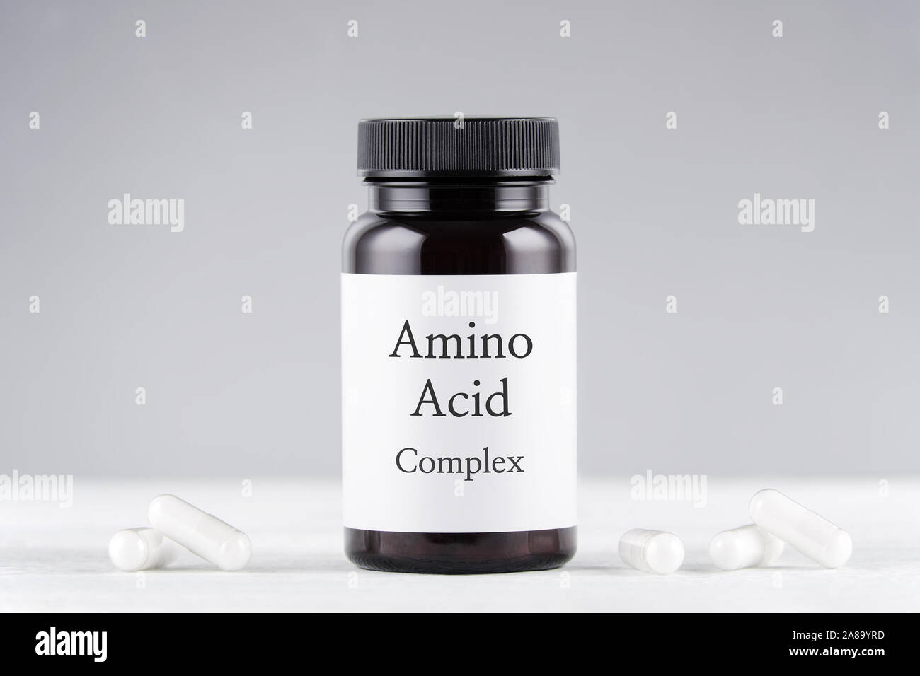 Suplemento nutricional de aminoácidos de botella y cápsulas sobre gris Foto de stock
