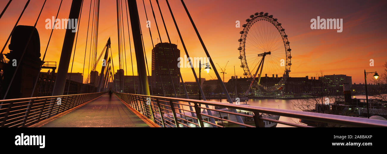 Puente que cruza un río con una rueda de Ferris en el fondo, el Jubileo de Oro de puente, el Río Támesis, Rueda del Milenio, la ciudad de Westminster, Londres, Inglaterra Foto de stock