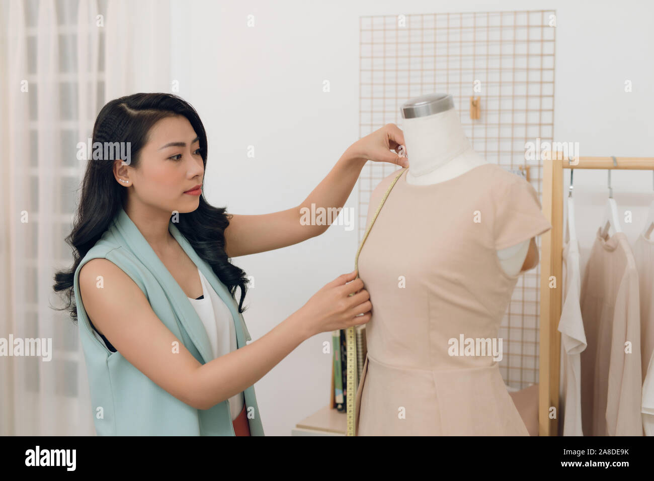 Diseñador de moda femenina joven asiático, tomando mediciones sobre el maniquí en su studio Foto de stock