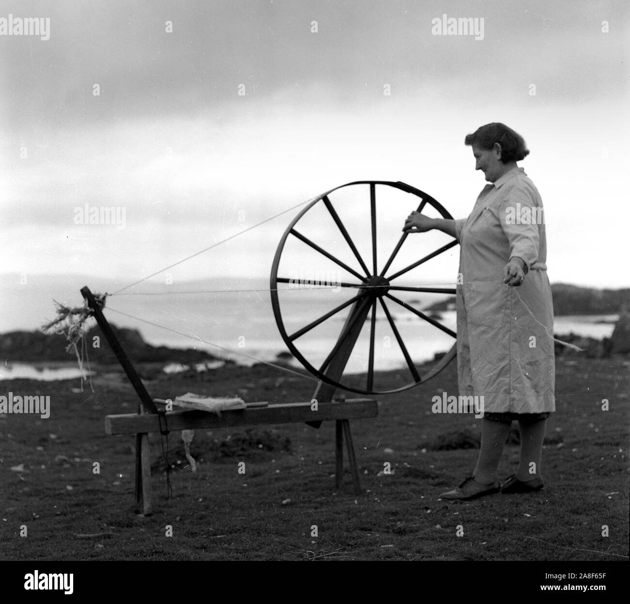 Señora con rueda giratoria girando un hilo de Galway, Irlanda 1955 Foto de stock