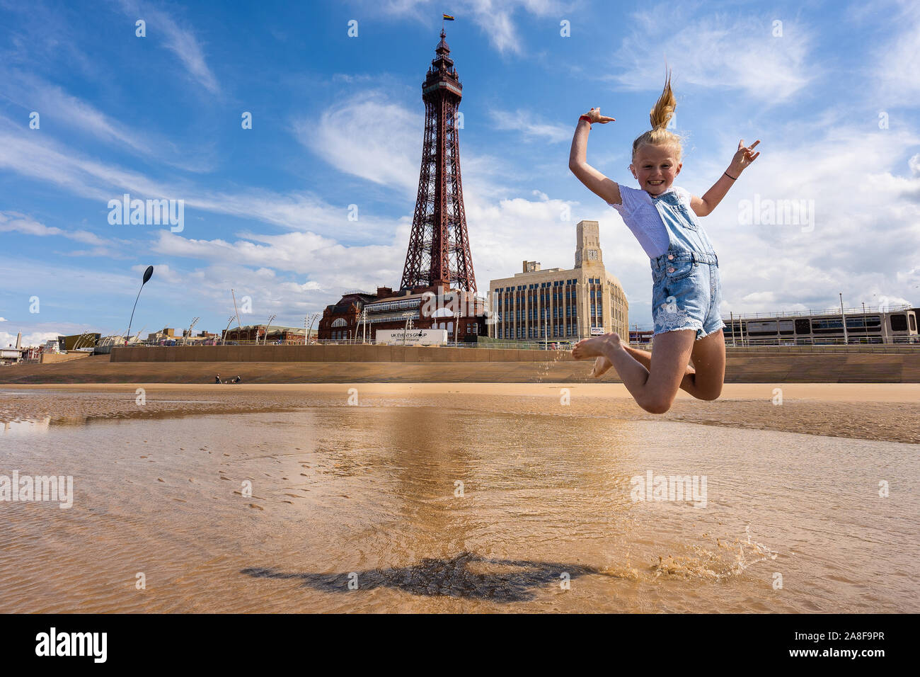 Una bonita niña vistiendo petos saltar alto en el aire de la playa de  Blackpool, con la famosa Torre de Blackpool, en el fondo, Turismo photogr  Fotografía de stock - Alamy