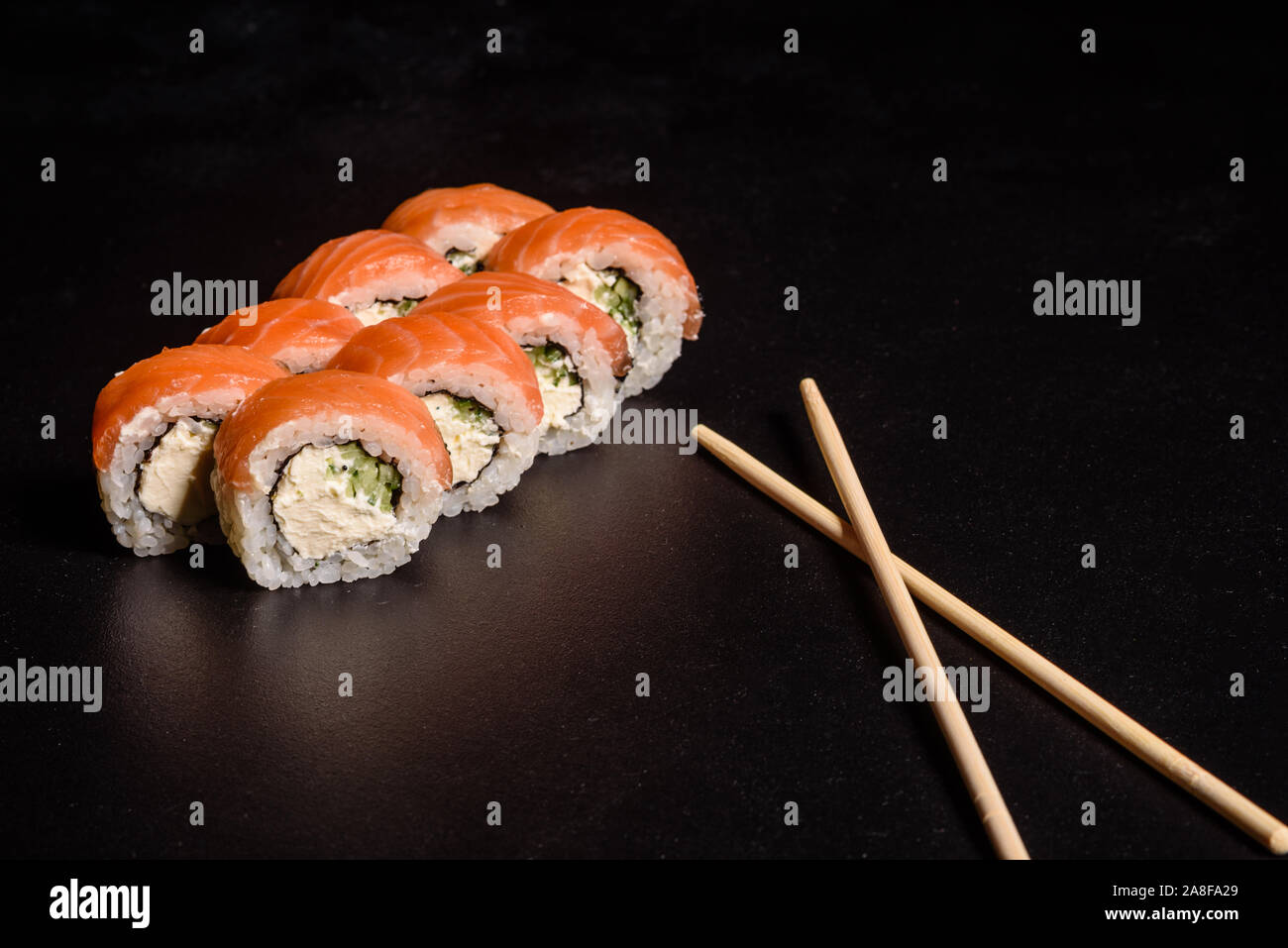 Diversos tipos de sushi servido sobre un fondo oscuro. Rollo con salmón, palta, pepino. Menú de sushi. La comida japonesa. Foto de stock