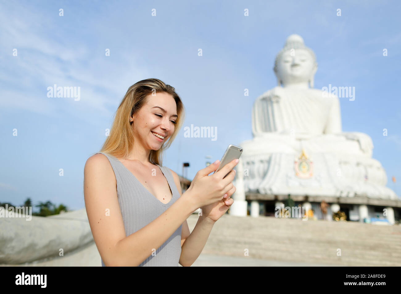 Joven Mujer hermosa conversando de smartphone cerca blanca estatua de Buda en Phuket. Foto de stock