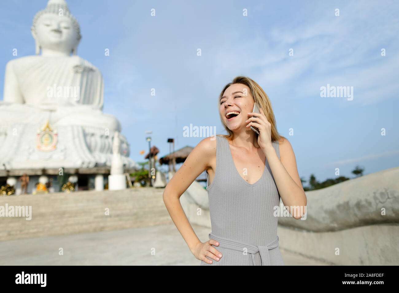 Chica sonriente joven hablando por teléfono inteligente cerca blanca estatua de Buda en Phuket. Foto de stock