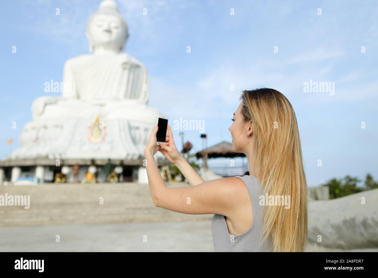 Joven Mujer rubia toma de fotografía de smartphone de blanca estatua de Buda en Phuket. Foto de stock