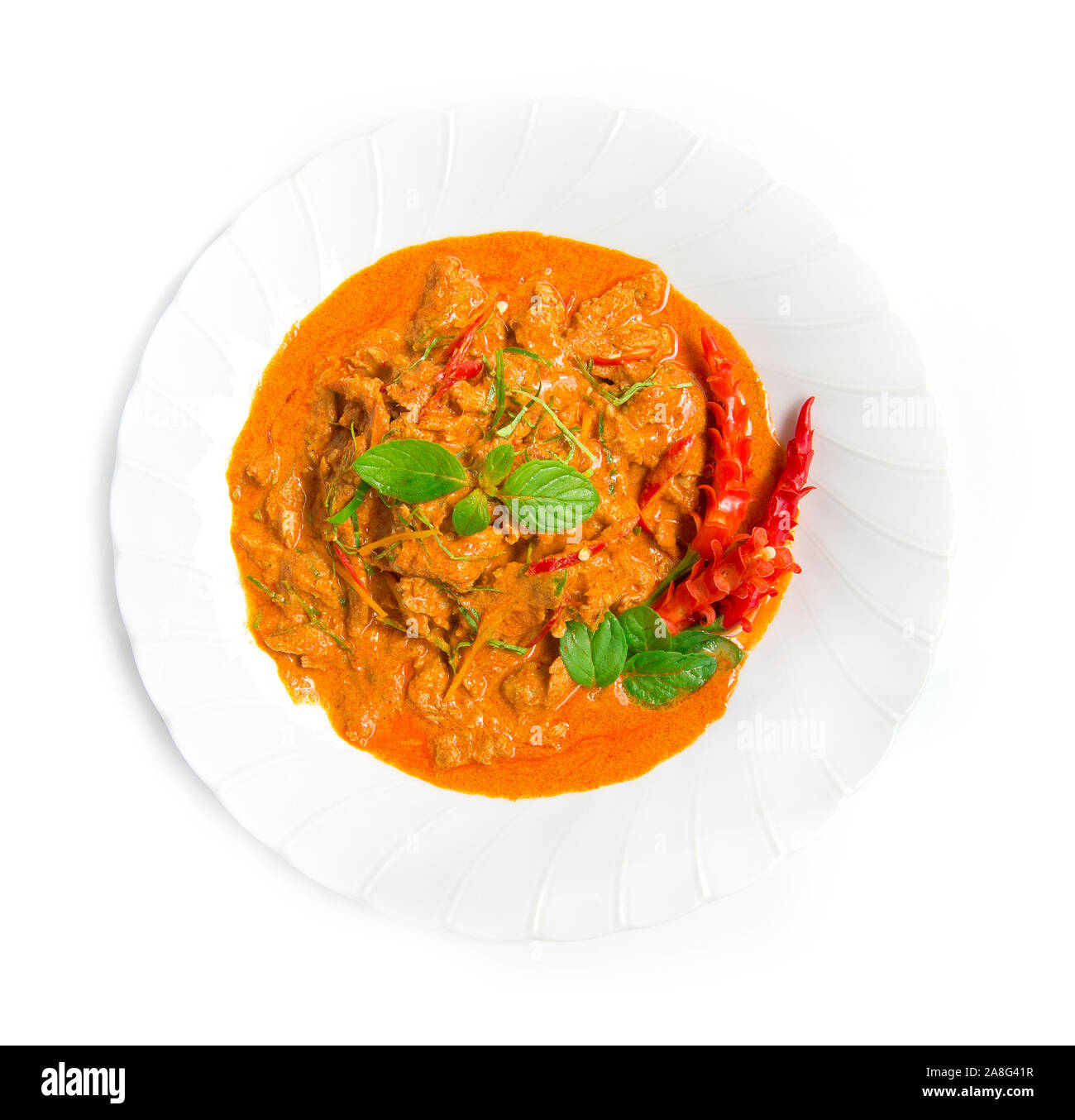 Curry rojo seco de cerdo con leche de coco (estilo curry Panang) Thaifood coronado con hojas de bergamota slice y chili vista superior aislado sobre fondo blanco. Foto de stock