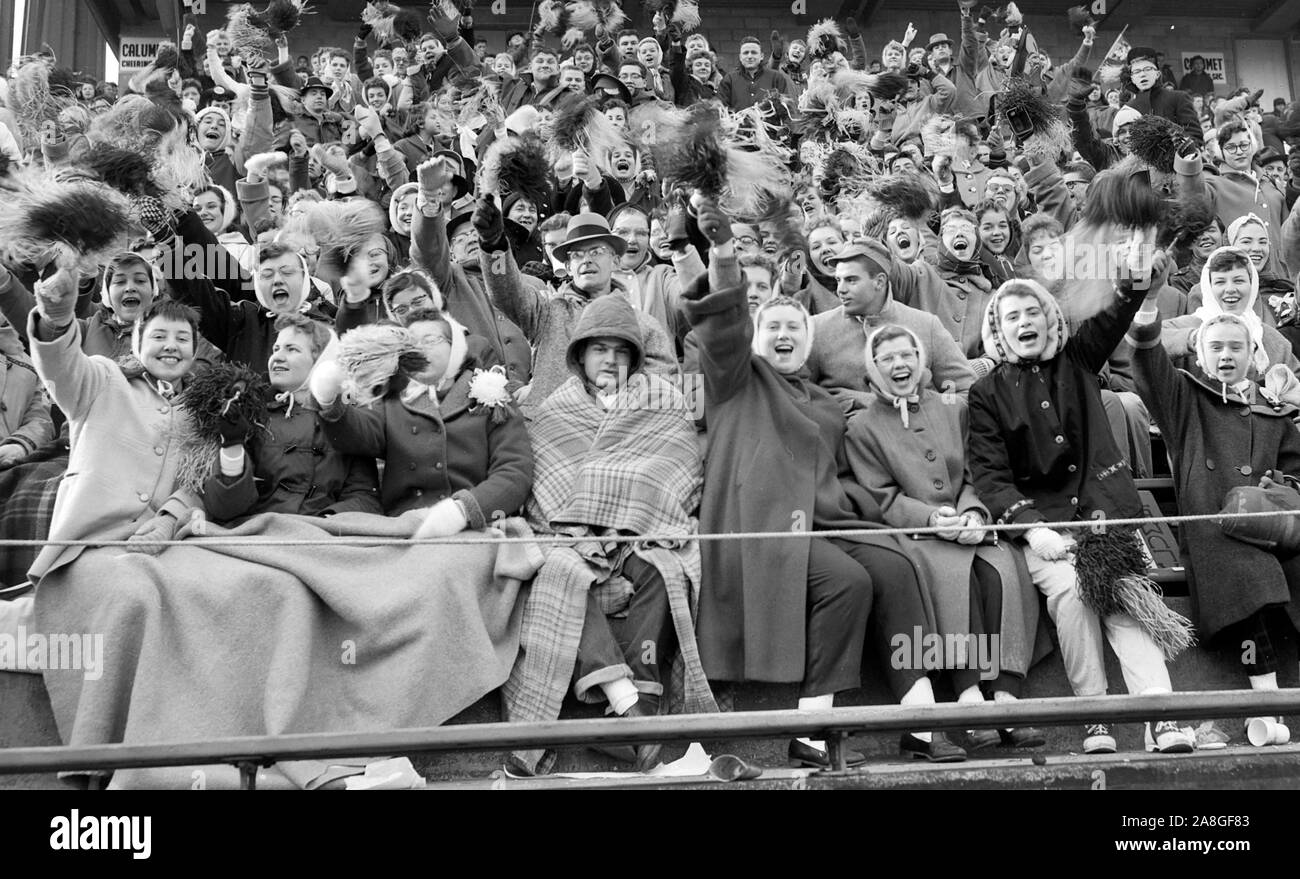 Ventiladores en el Chicago's Soldier Field están agrupados en el frío para animar a su equipo durante un campeonato estatal de alta escuela de fútbol, ca. 1955. Foto de stock