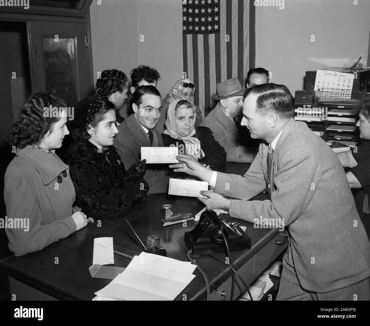 Un grupo de inmigrantes se agolpan alrededor de una mesa en el Servicio de Inmigración y Naturalización en Chicago para recibir los formularios correspondientes, ca. 1953. Foto de stock