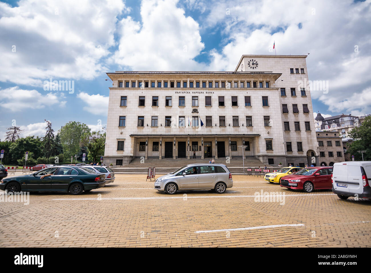 Sofia, Bulgaria - Junio 25, 2019: el tráfico de coches en frente del edificio del Banco Nacional Búlgaro en un día soleado Foto de stock