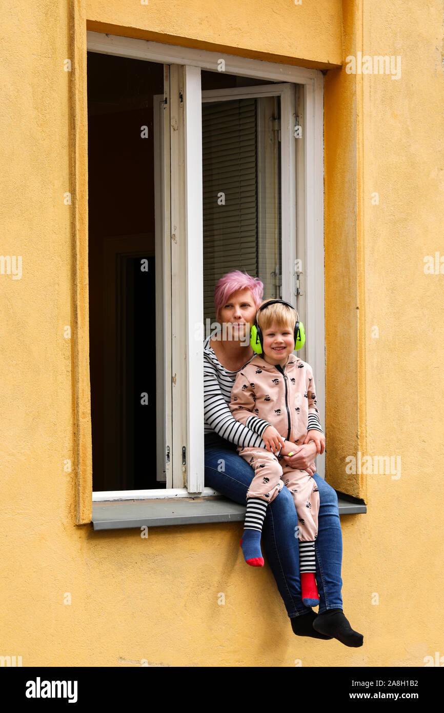 Madre e hijo con protección auditiva sentado en el piso bajo la repisa de la ventana durante Kallio Block Party 2019 en Helsinki, Finlandia Foto de stock