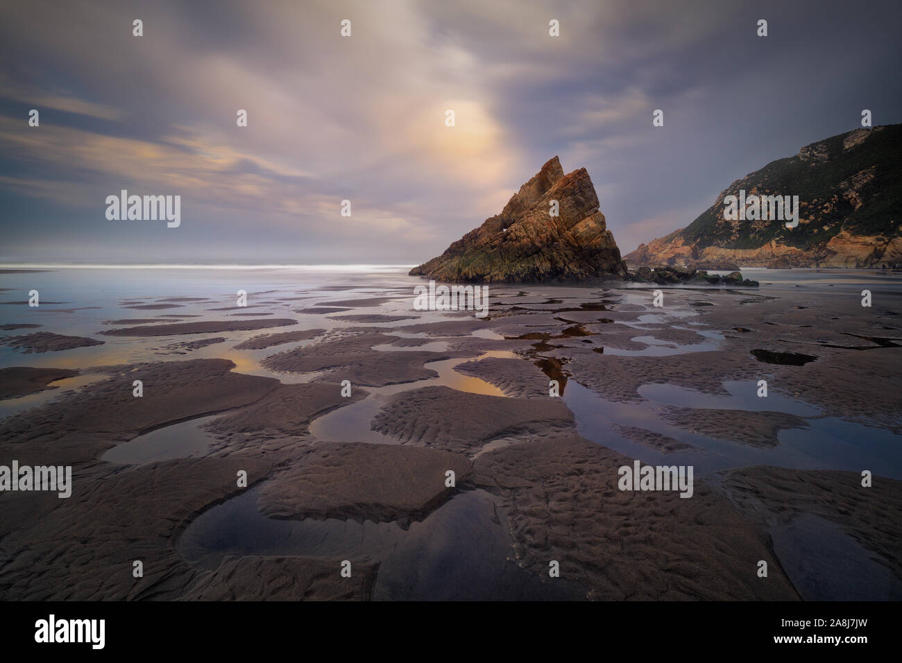 Formación de roca triangular y patrón reflexiones sobre la arena, en una playa de Asturias, la costa cantábrica, en España. Playon de bayas. Nuboso por la mañana. Foto de stock