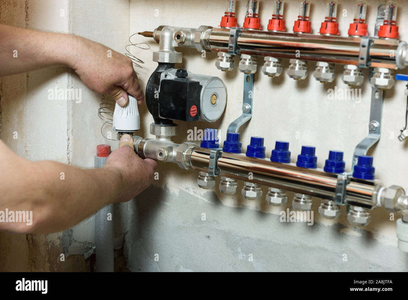 Un trabajador es instalar una cabeza térmica en el hogar sistema de calefacción distribuidor. Foto de stock