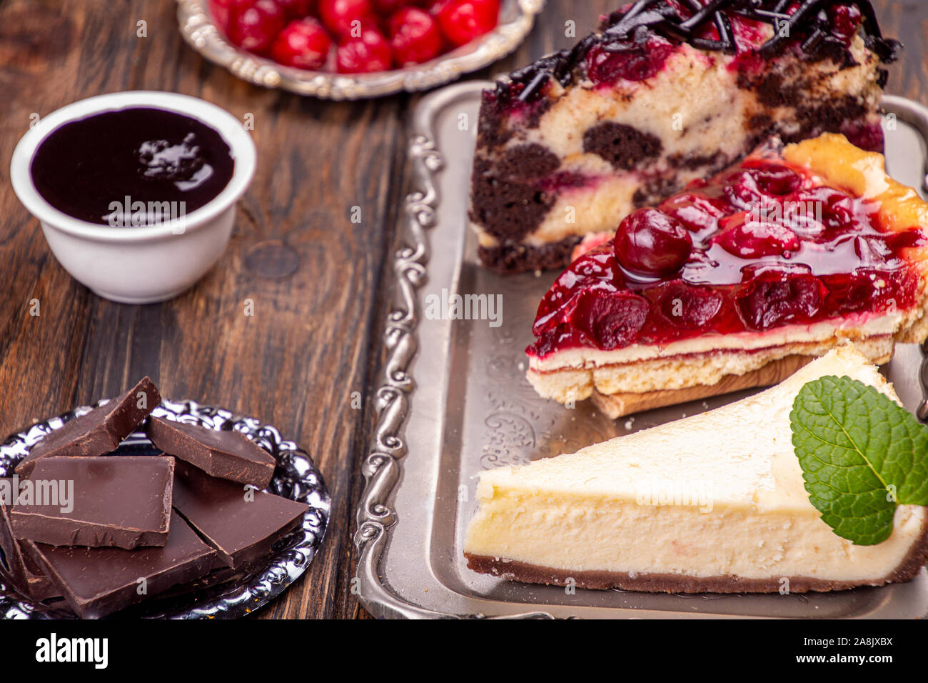 Cherry Chocolate pastel de frutas, cerezas y cheesecake cheeseccake en  bandeja de plata tres trozos de tartas dulces sobre fondo blanco de madera  Fotografía de stock - Alamy