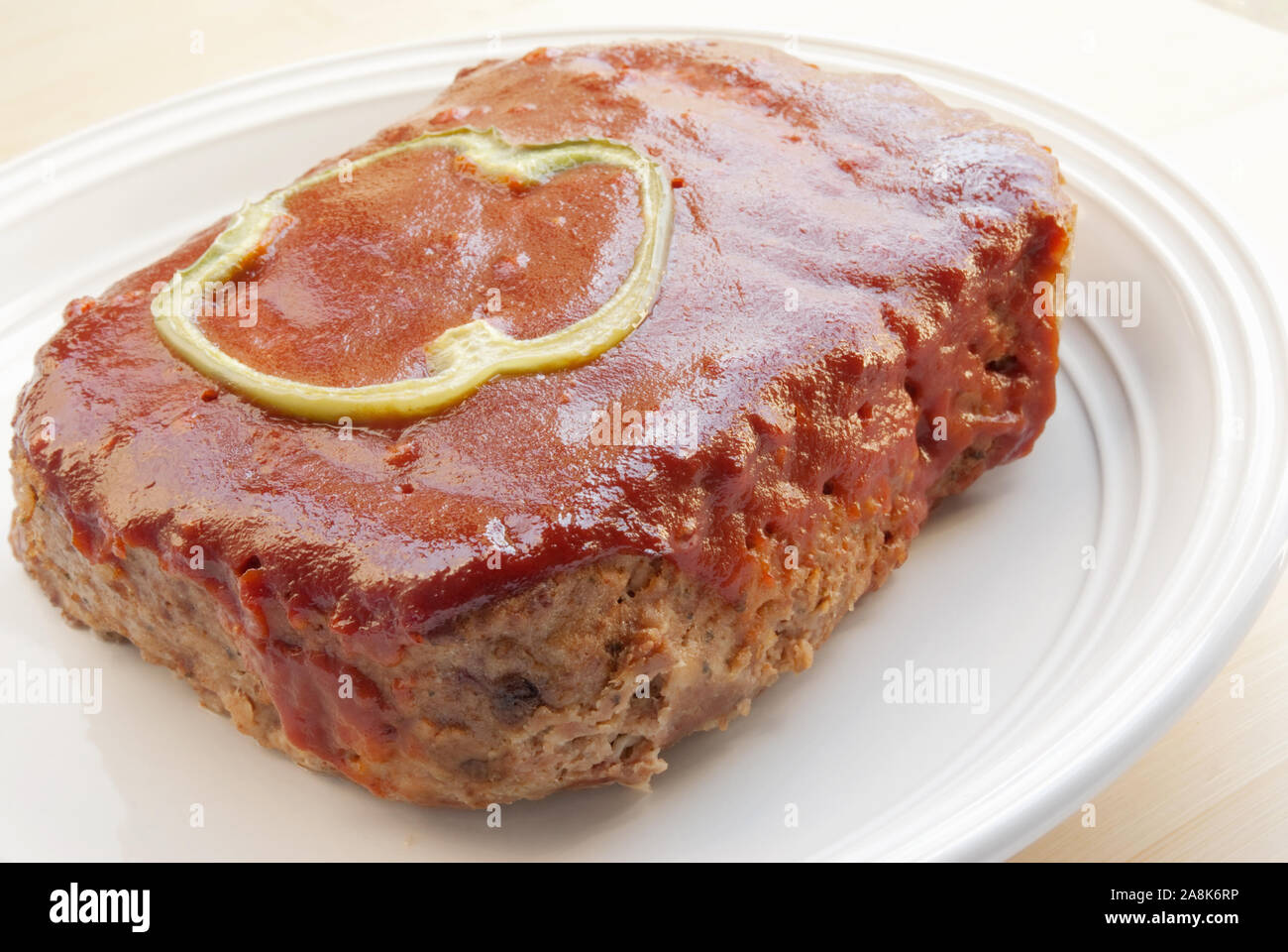 Recién horneados caseros Meat Loaf, coronado con un trozo de pimiento verde y una salsa base de ketchup. Esta deliciosa comida es servida en una cerámica blanca pl Foto de stock