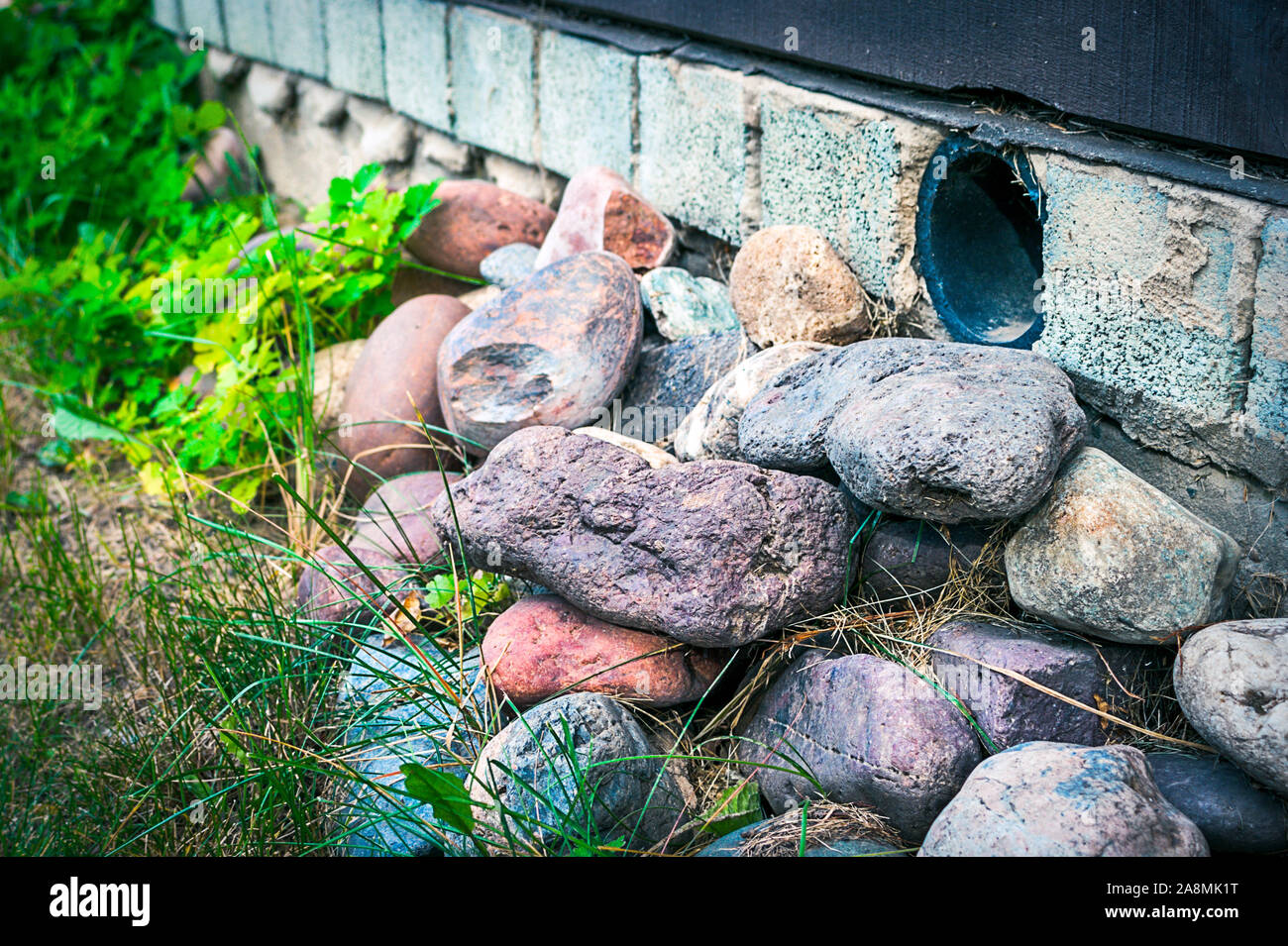 Montón de coloridas rocas cerca de una casa Fundación con ventilación de tuberías de plástico para asegurar la circulación del aire bajo el suelo y prevenir el moho y la podredumbre. Foto de stock