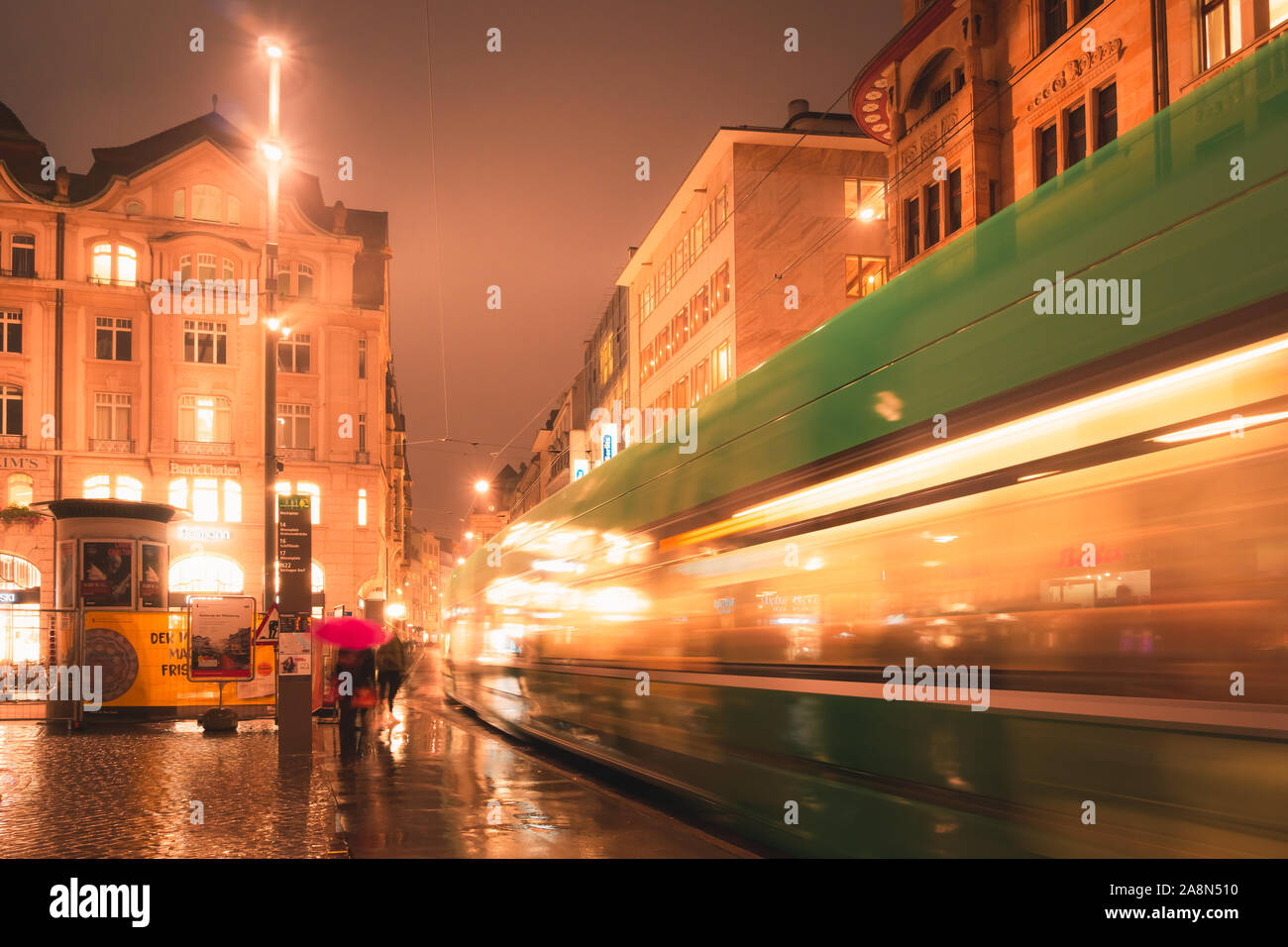 Escena nocturna urbana en una noche lluviosa con tranvía en movimiento y luces brillantes, Basilea Marketplatz downtown, Suiza. Foto de stock