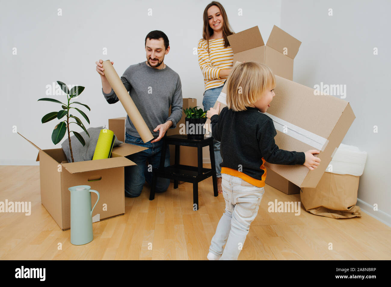 Joven familia se mudó a una nueva casa, desembalaje de cajas de cartón junto Foto de stock