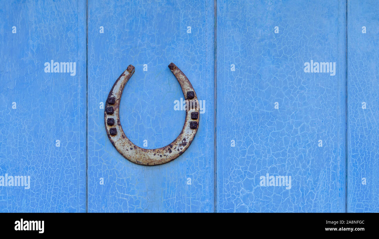 El hierro viejo suerte con clavos de herradura, termina hacia arriba para  atrapar la suerte, un talismán de protección, en una puerta de madera azul  vintage con la pintura descarapelada agrietado Fotografía