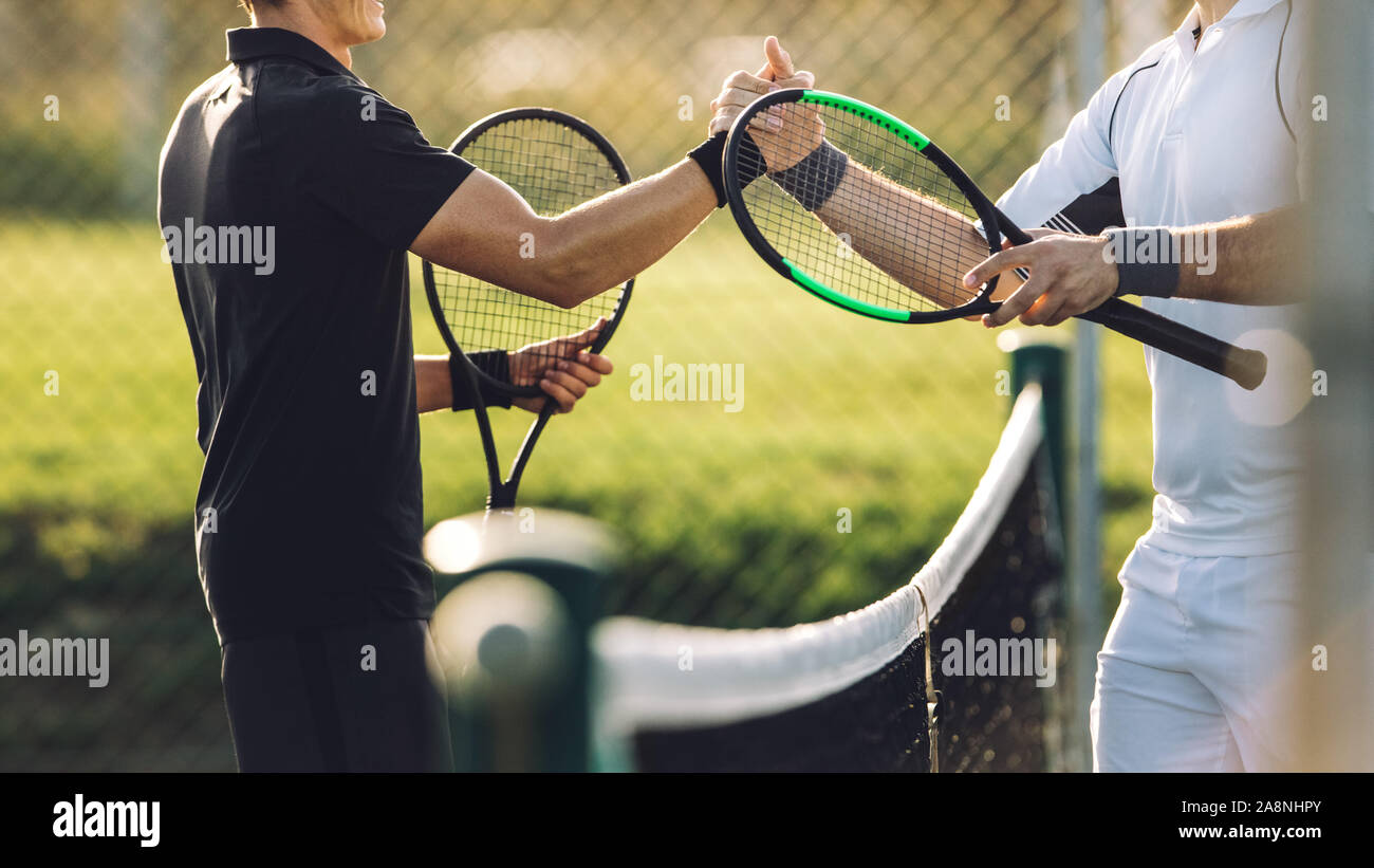 Dos joven agitando las manos después de jugar al tenis. Los jugadores de tenis se estrechan las manos por encima de la red después del partido. Foto de stock