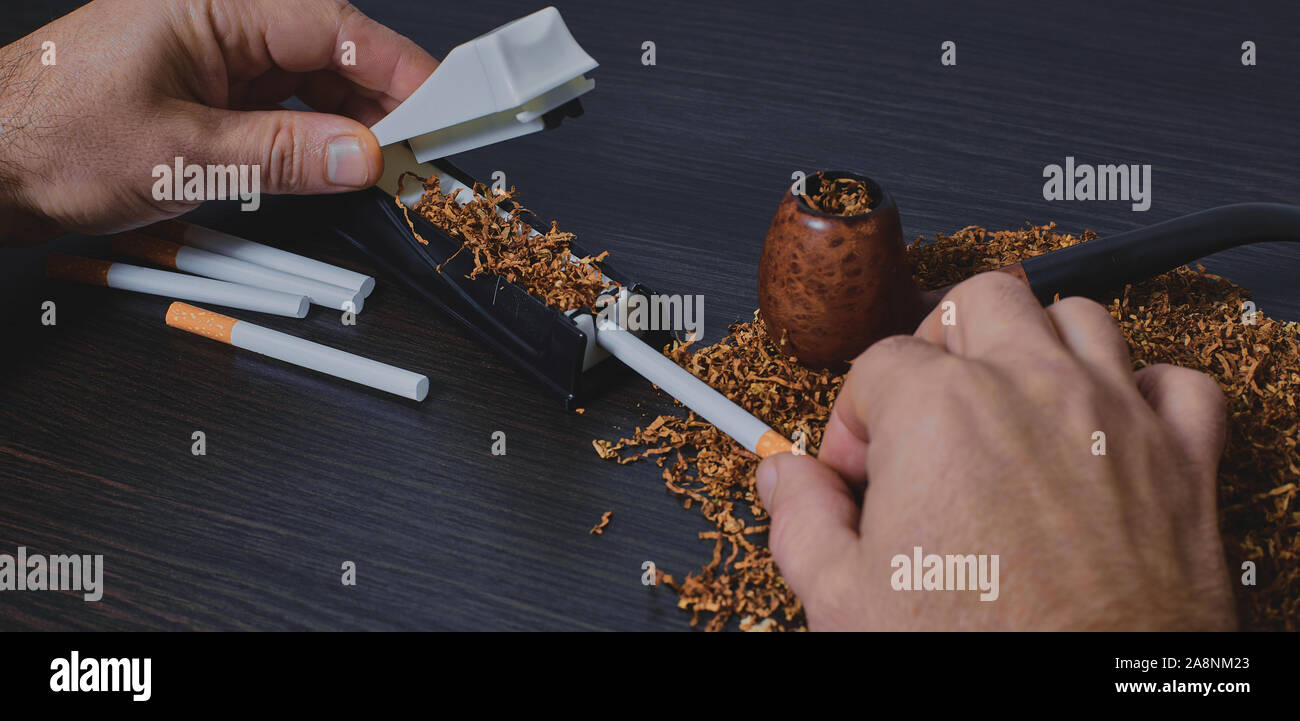 El hombre hace un cigarrillo con máquina laminadora, manos closeup Foto de stock