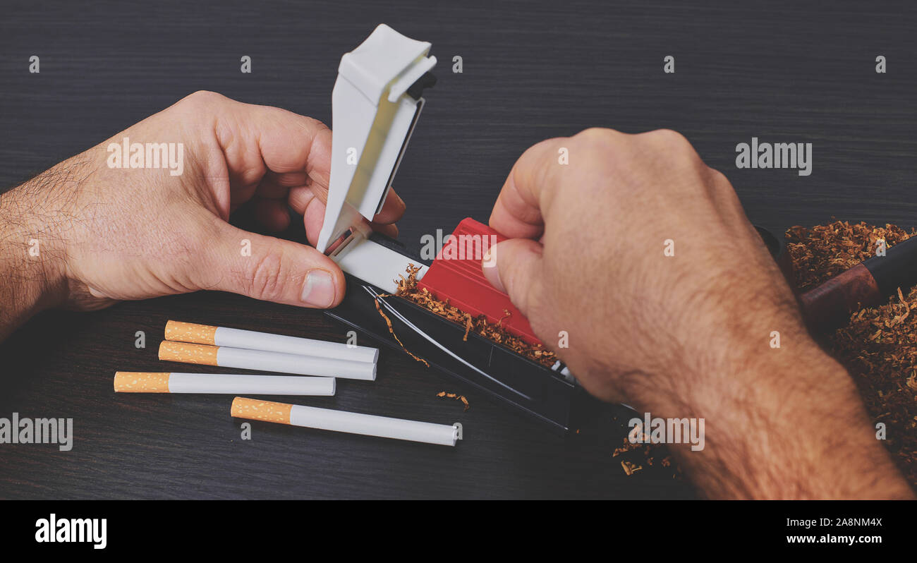 El hombre hace un cigarrillo con máquina laminadora, manos closeup Foto de stock