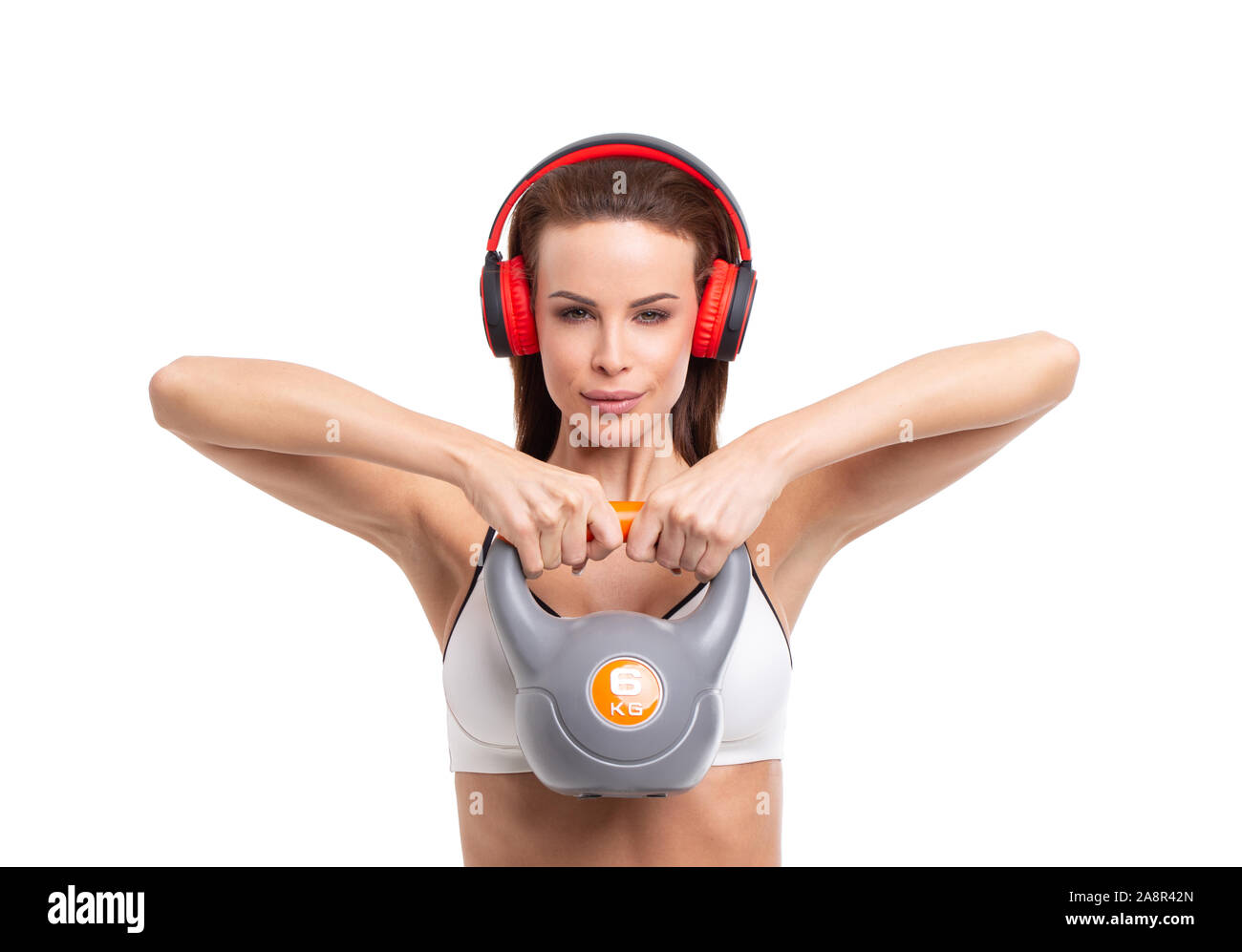 Joven mujer deportiva en auriculares celebración kettlebell aislado en blanco Foto de stock