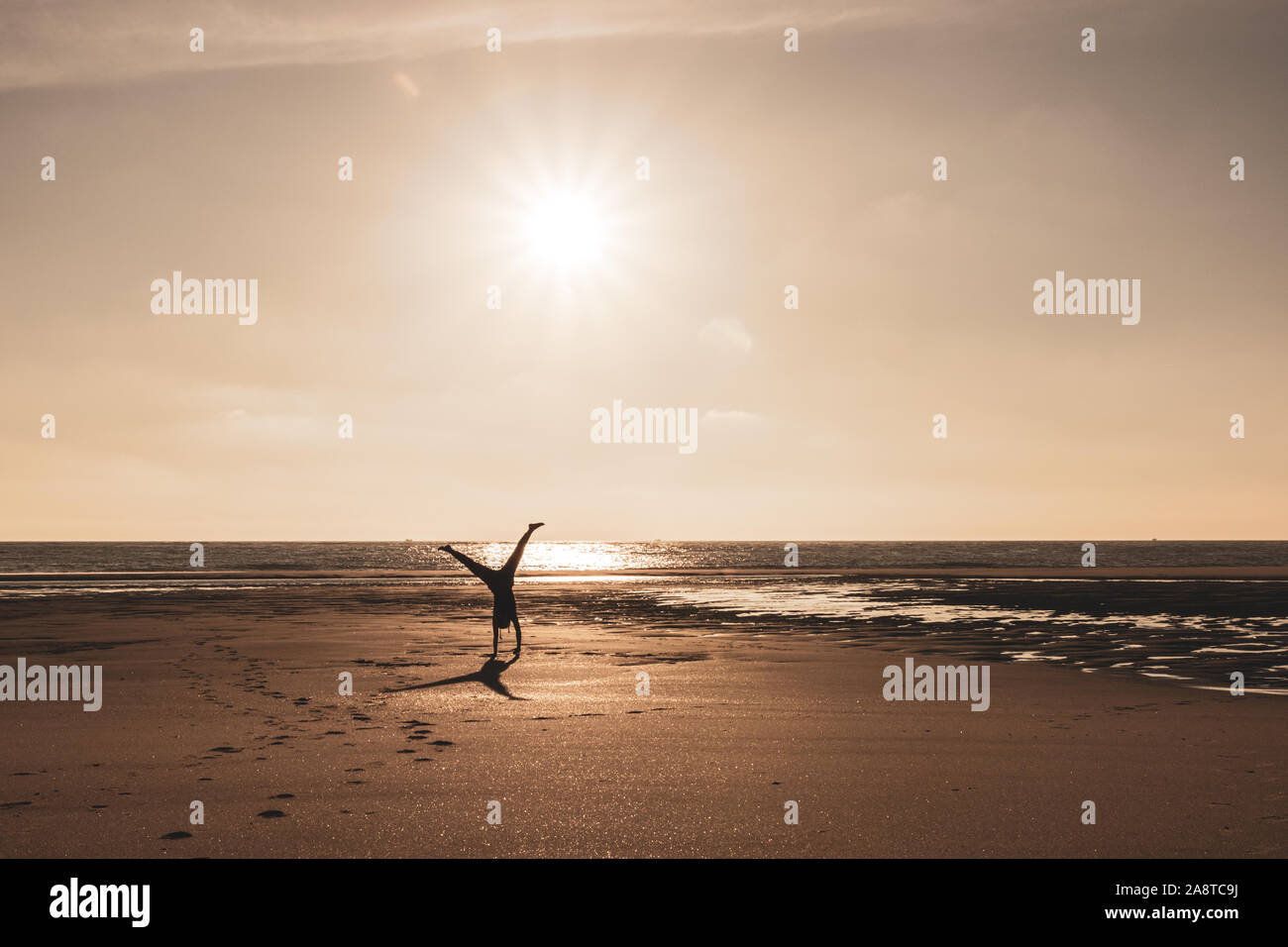 Una mujer haciendo un cartwheel en una playa de Fuerteventura, España al atardecer Foto de stock