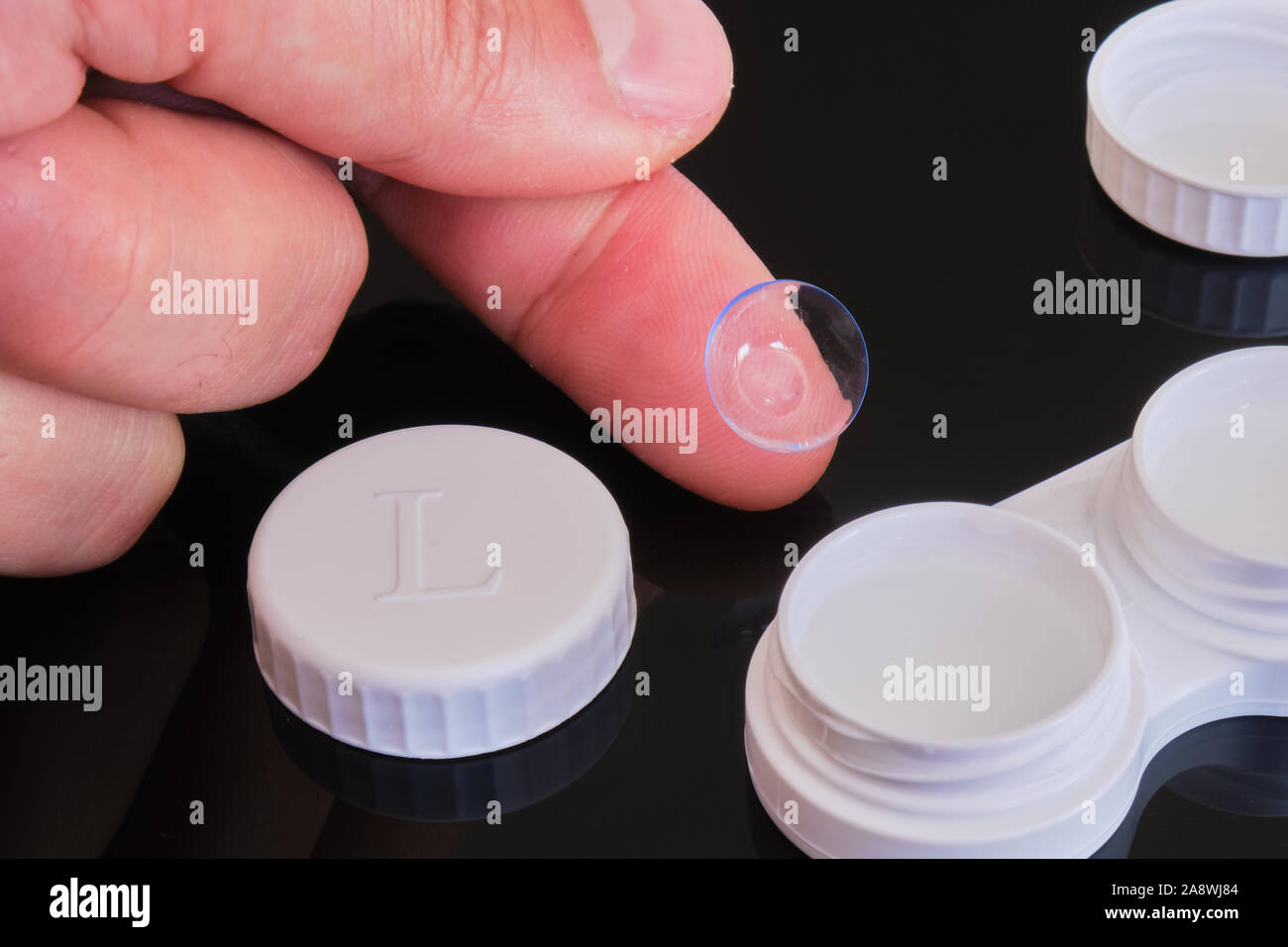 Lentes de contacto tóricos de fingertip con blanco y tapa de lente de  contacto caso - composición negra sobre fondo reflectante Fotografía de  stock - Alamy