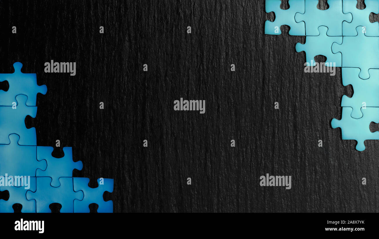 Puzzle azul en las esquinas de la imagen sobre un fondo negro de piedra natural de pizarra. Un bastidor con un espacio vacío para su descripción. Foto de stock