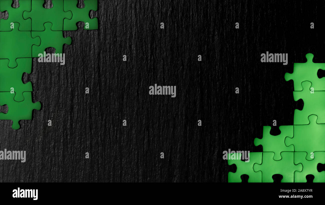 Puzzle verde en las esquinas de la imagen sobre un fondo negro de piedra natural de pizarra. Un bastidor con un espacio vacío para su descripción. Foto de stock