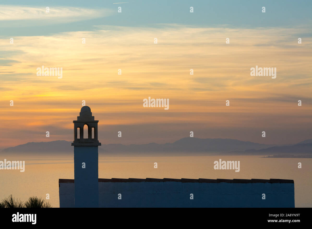 Una casa tradicional con chimenea ornamental se recortaba contra el atardecer en la punta de la Mona mirando a través de la bahía de La Herradura en Almuñécar, España. Foto de stock