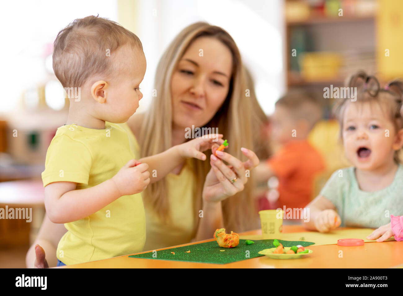 Linda mujer y a los niños jugar con juguetes de arcilla en el centro de cuidado diurno Foto de stock