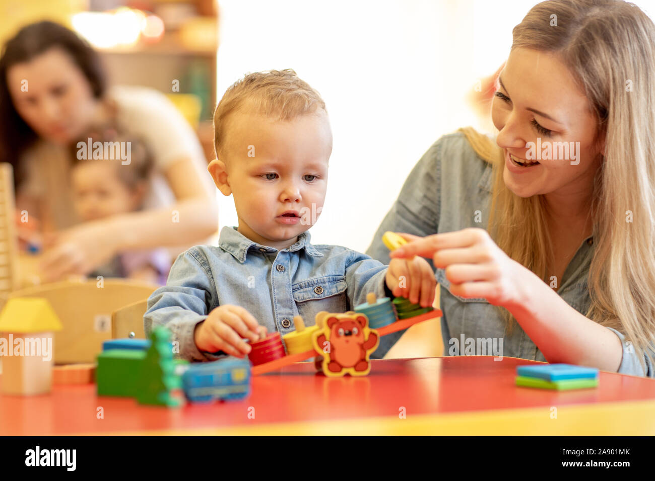 Los niños con los maestros jugando con color madera rompecabezas en un aula montessori Foto de stock
