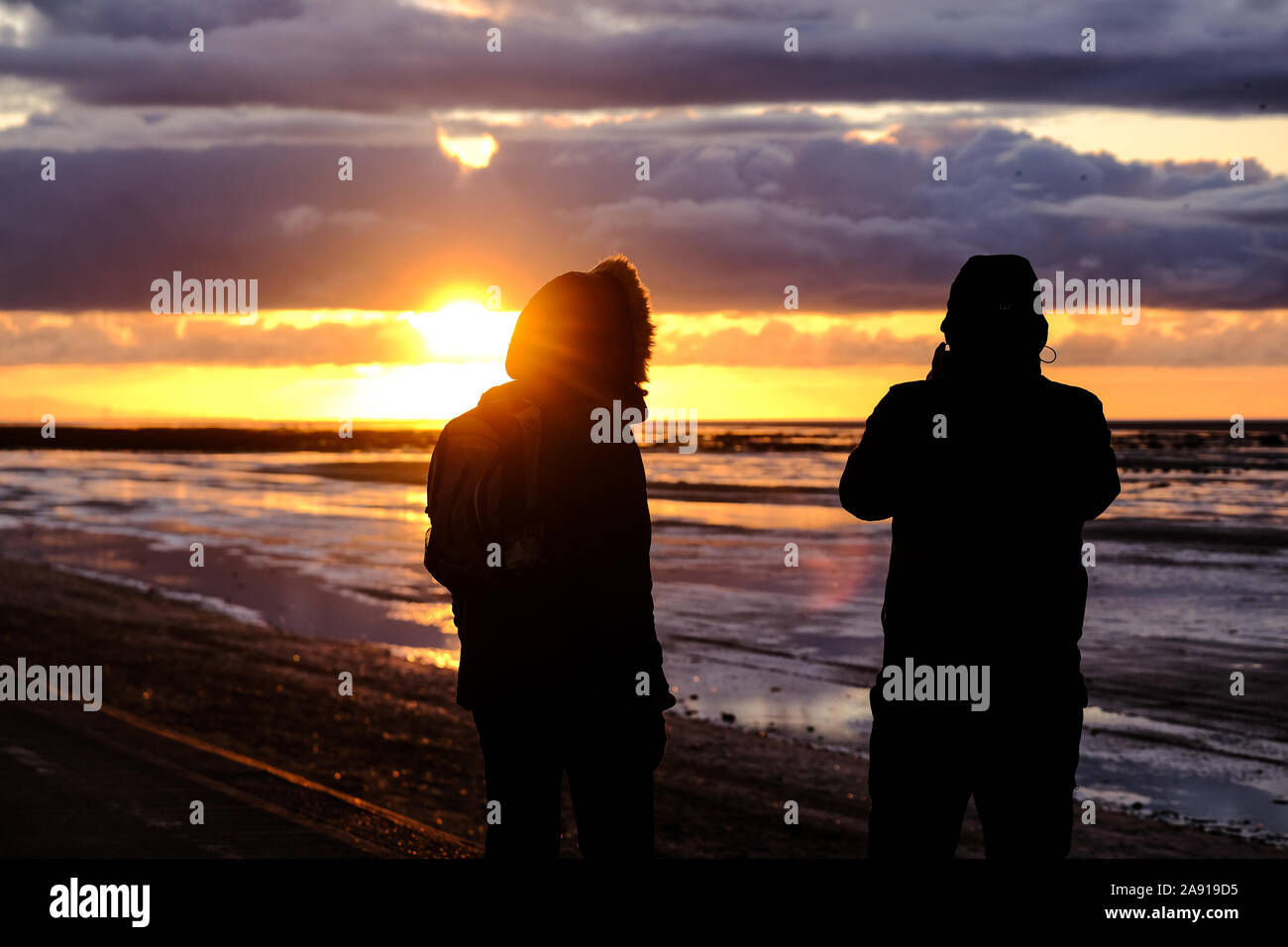 Una pareja viendo la puesta de sol en la costa de Southport, en el noroeste de Inglaterra. Foto de stock