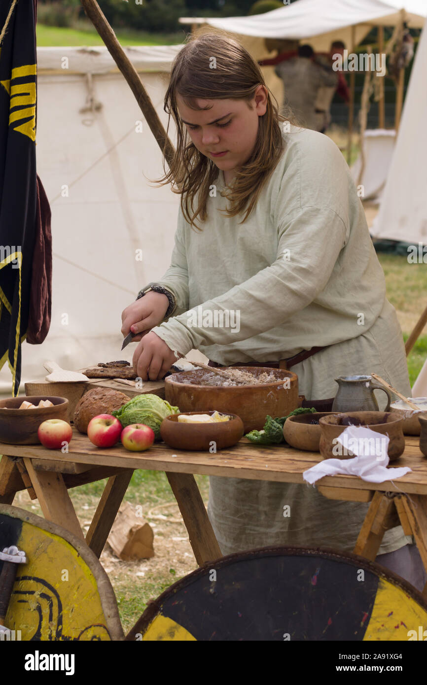Mujer vestida con traje medieval preparando la comida en una nueva promulgación de camp Foto de stock